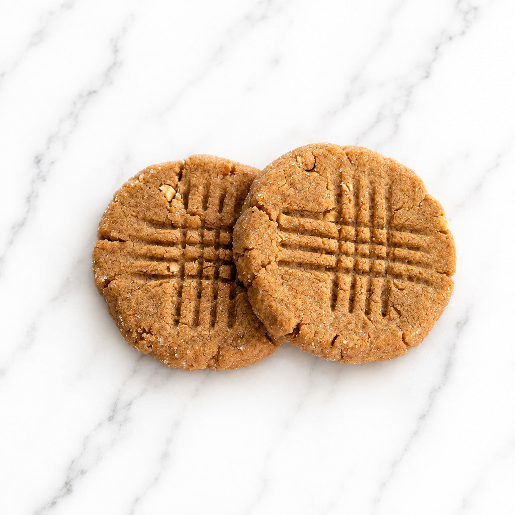 Two Peanut Butter Reserve cookies from TNT Sweets made with Madasgar vanilla on a white marble surface.