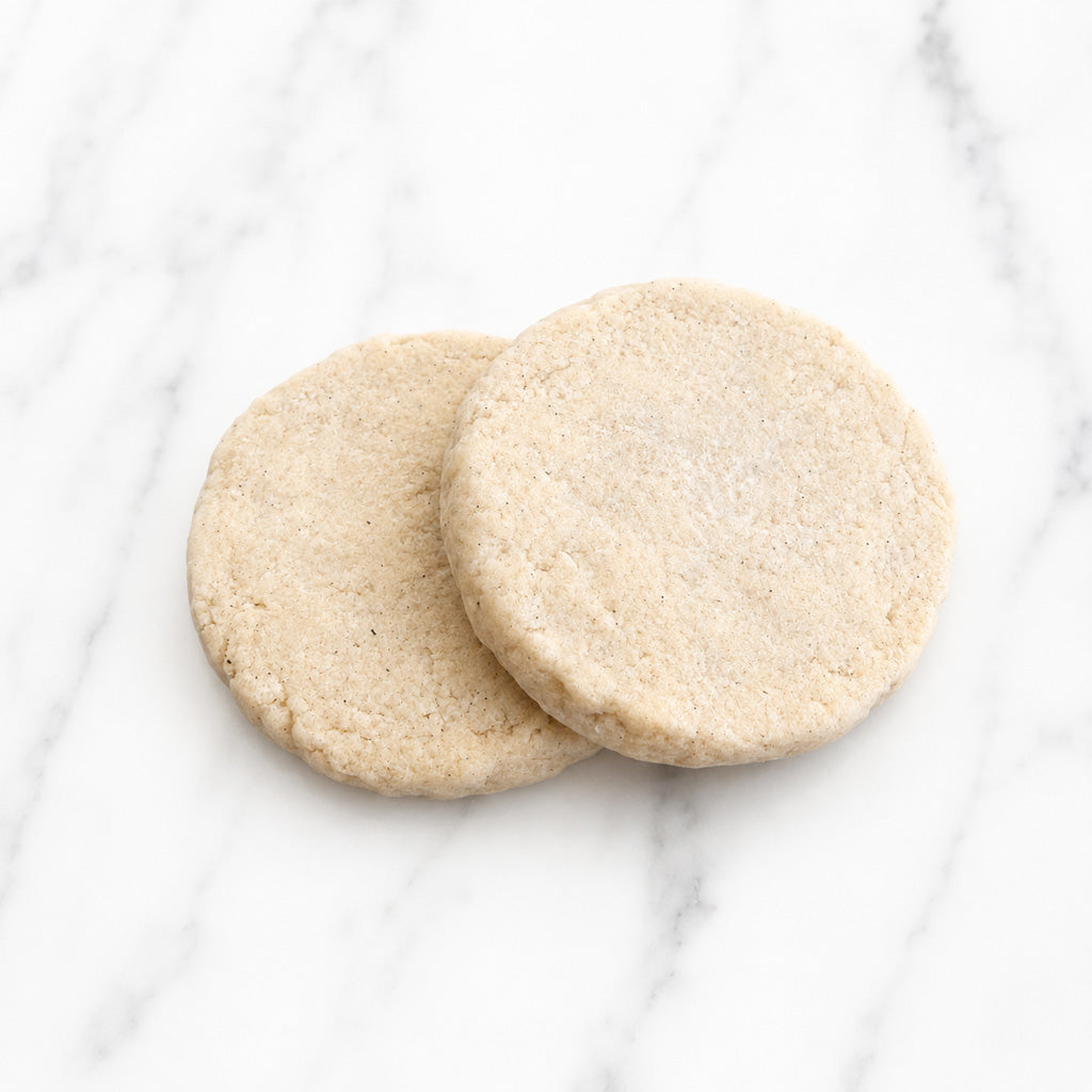Two The Première vanilla bean shortbread cookies on a white marble background.