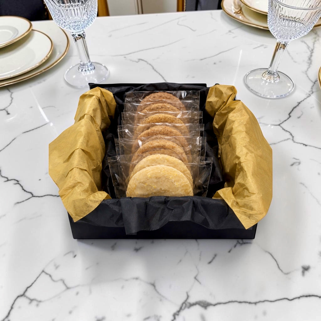 The Quartet by TNT Sweets presented in an open black keepsake box with individually wrapped cookies nestled in black and gold tissue. 