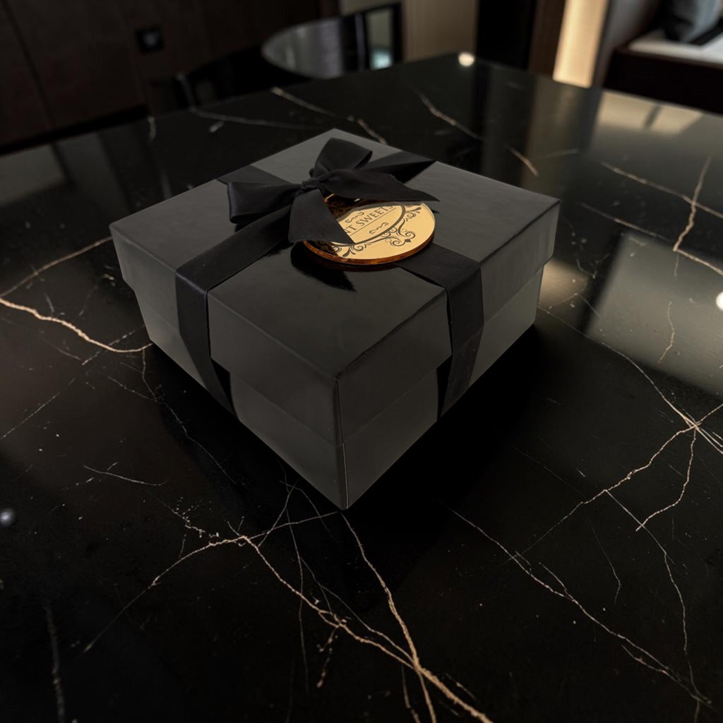 The Quartet by TNT Sweets presented in a closed black keepsake box with black satin ribbon and gold logo medallion.
