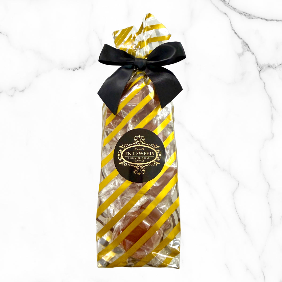 Caramels in a gold and white striped design and black bow on a marble background.