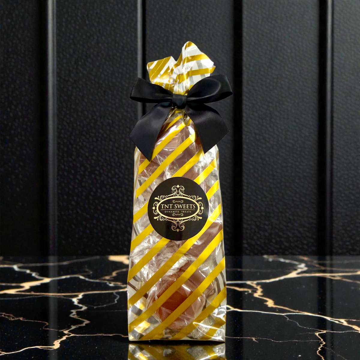 Caramels in a gold striped bag with a black bow on a black and gold marble countertop.