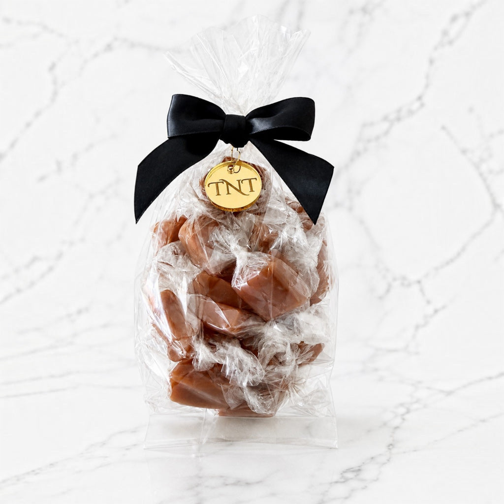 Clear half-pound bag of The Velvet Heat cayenne sea salt caramels, finished with a black satin bow and gold TNT medallion.