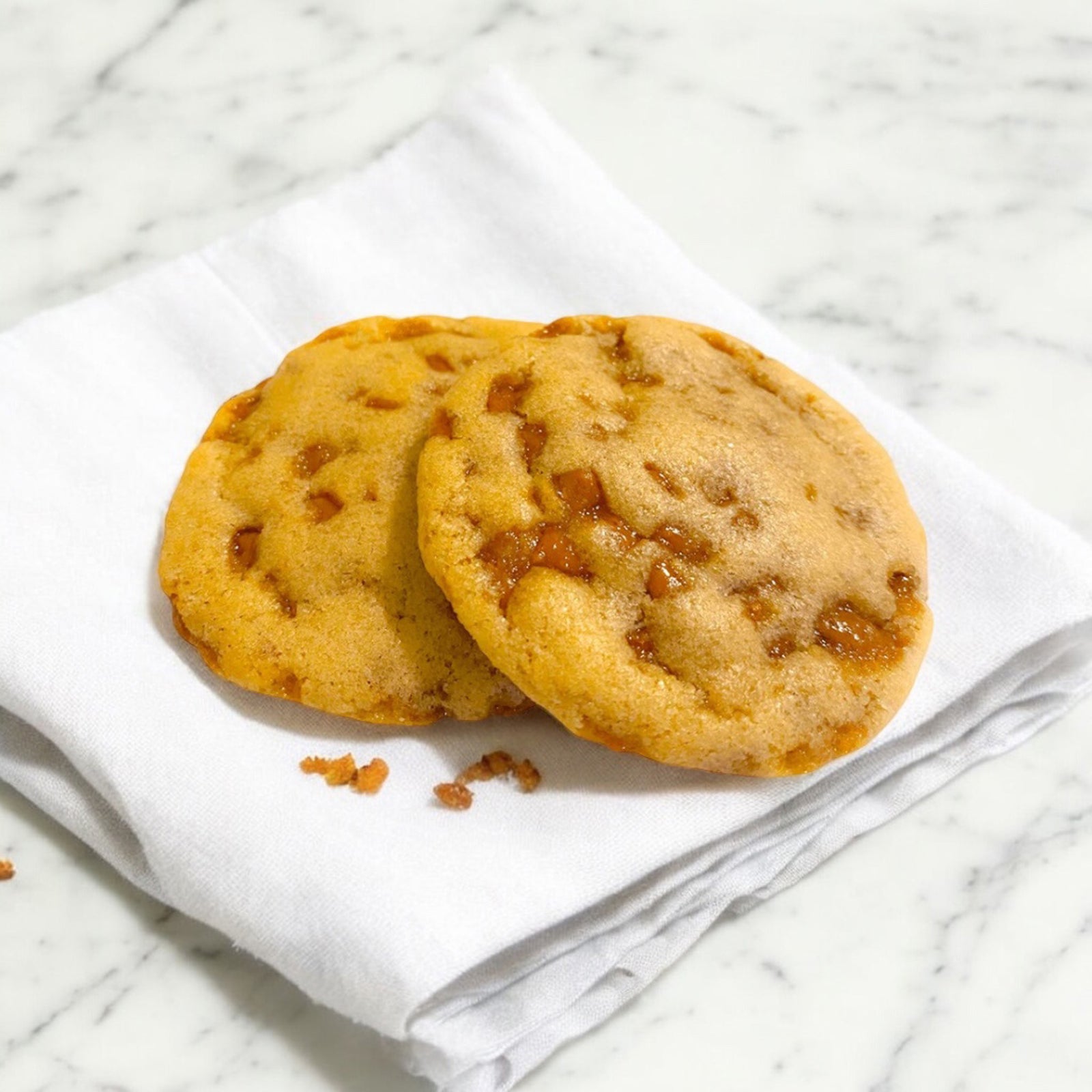 TNT toffee cookies on a white linen napkin on a white marble counterop.
