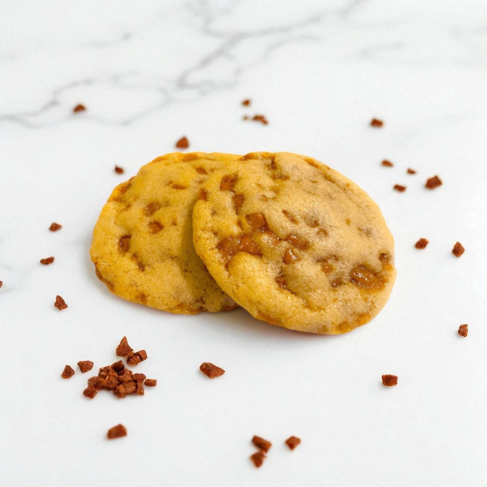 Two toffee royale cookies with caramel bits on a white marble surface.