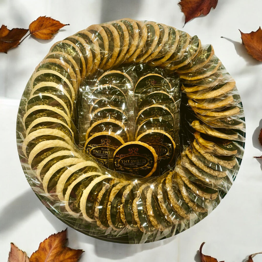 An assortment of five dozen cookies on a black cookie platter on a wooden countertop with scattered fall leaves.