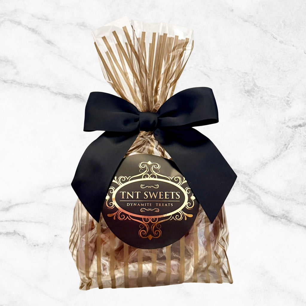One pound of Velvet Heat Cayenne Caramels from TNT Sweets in the Gold Stripe Wrap with a black satin bow finished with the TNT Sweets signature seal on a white marble background.