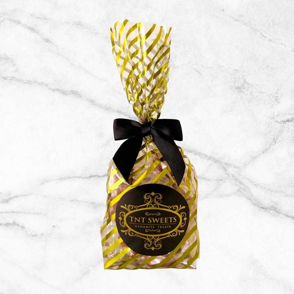 Half-pound Velvet Heat Cayenne Caramels from TNT Sweets in the Gold Strip Wrap with a black satin bow and signature TNT Sweets seal on a white marble background.