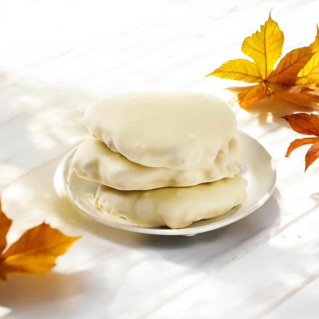 Stack of three white chocolate chews on a white plate on a wooden countertop with scattered fall leaves.