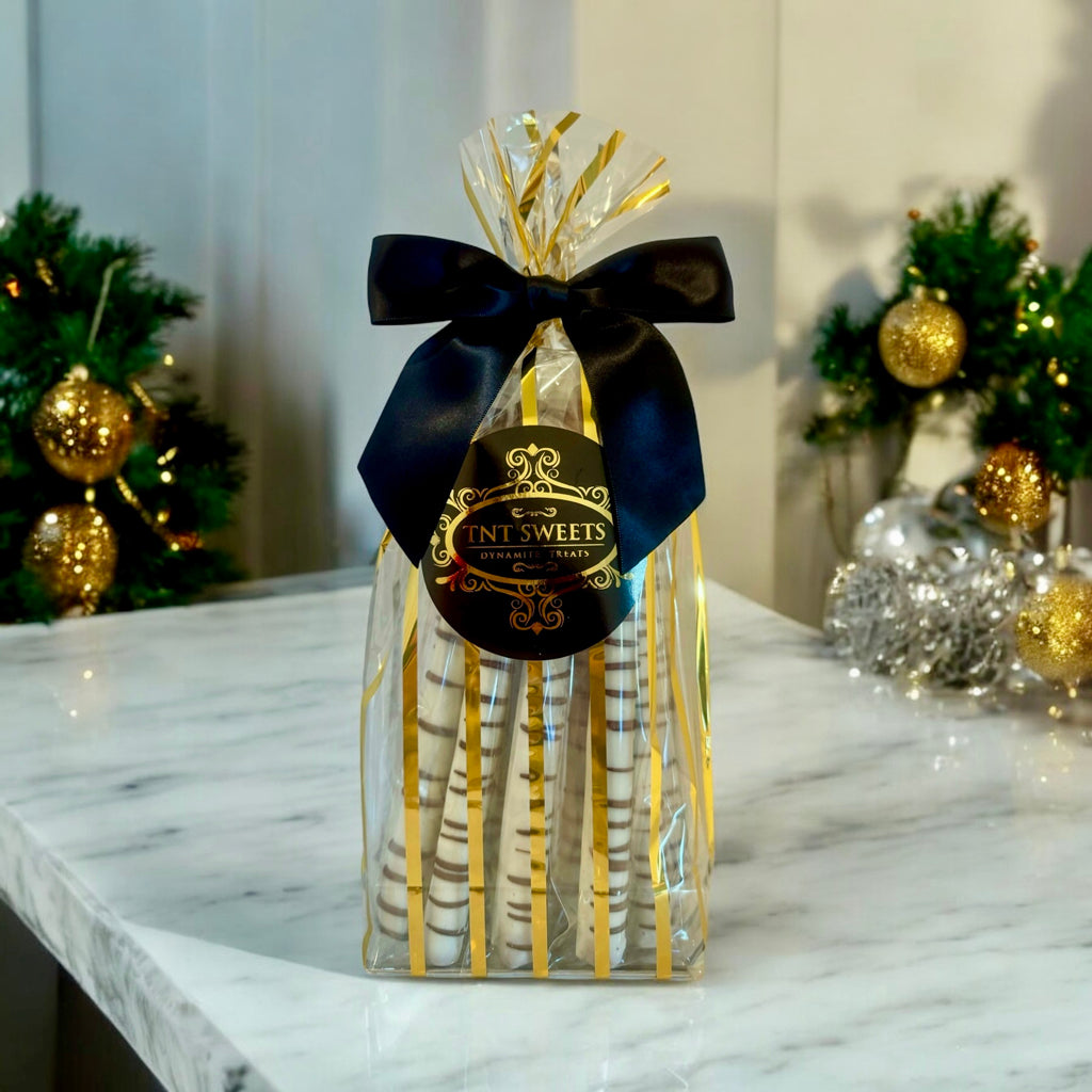 One dozen white chocolate pretzels on a dark wooden countertop with pine holiday decor.