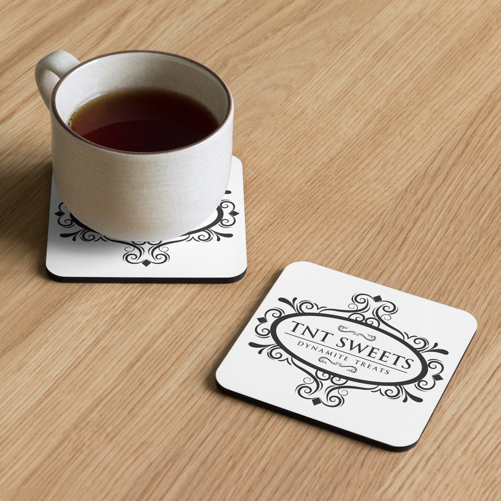 Two classic white TNT coasters with a black logo on a wood countertop with a cup of coffee sitting on one coaster.