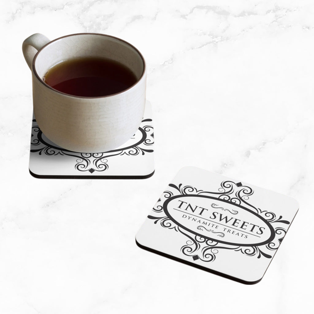 Two classic white TNT coasters with a black logo on a marble countertop with a cup of coffee sitting on one coaster.