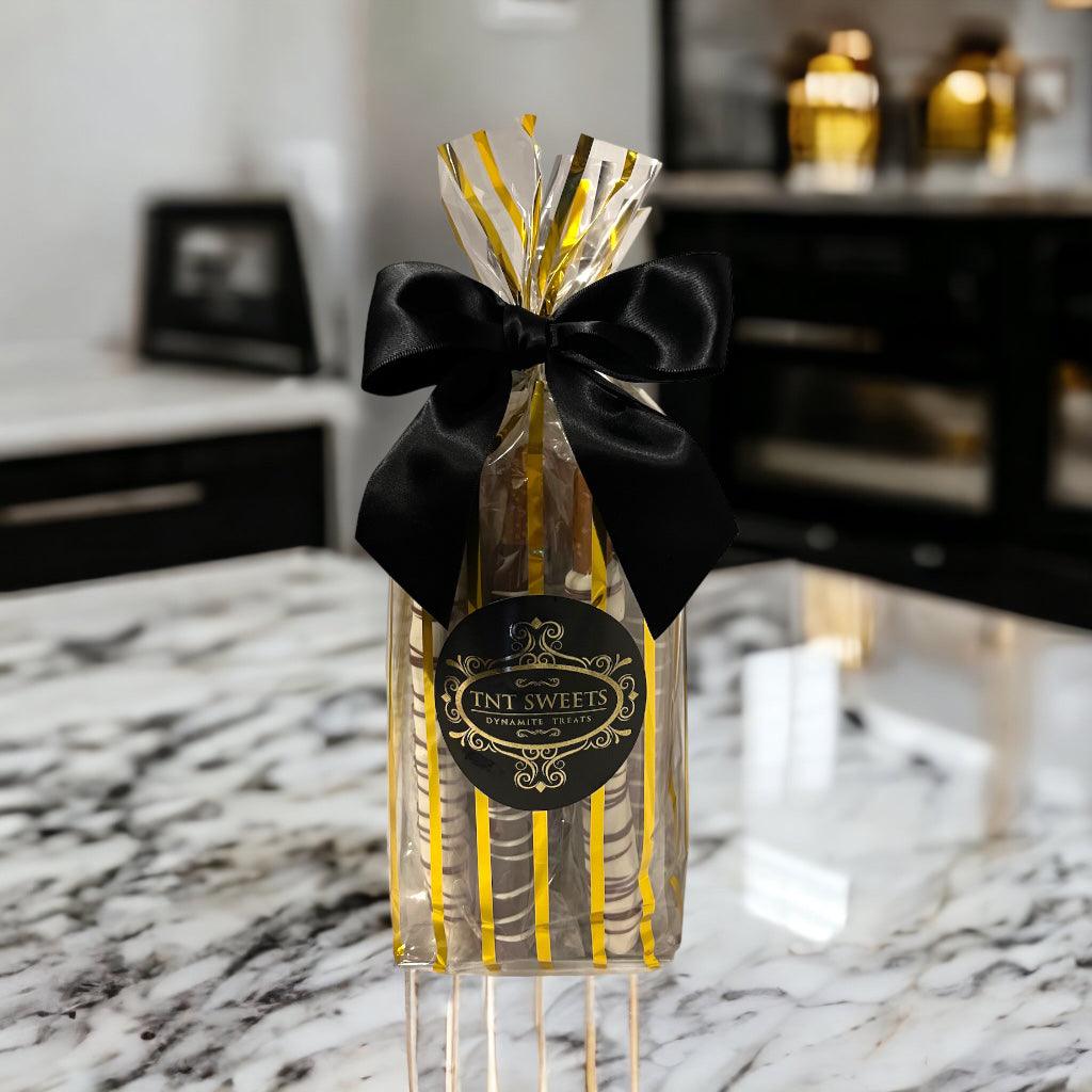 White chocolate, milk chocolate and dark chocolate pretzels in a gold striped gift bag with a black bow on a marble countertop.