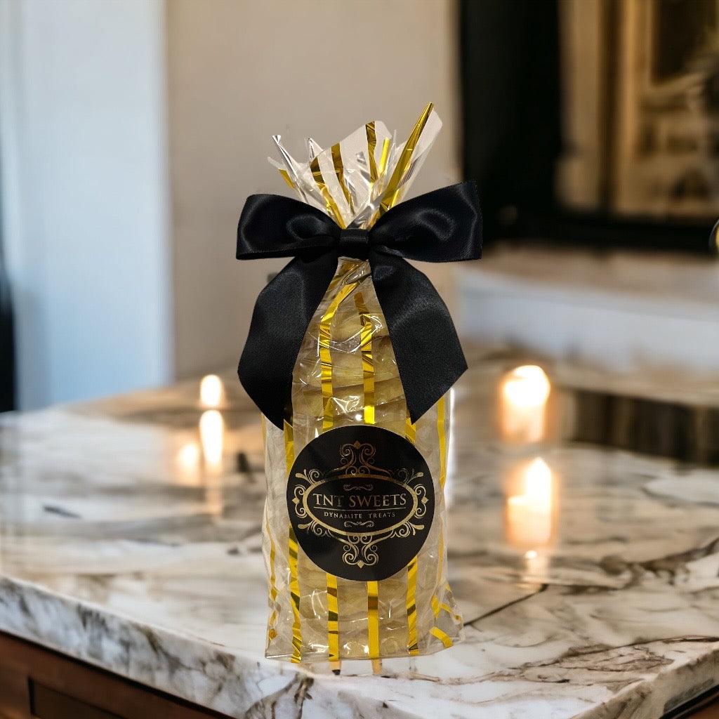 Lemon glazed cookies in a gold striped gift bag with a black bow on a marble countertop blurred background and candlelight.